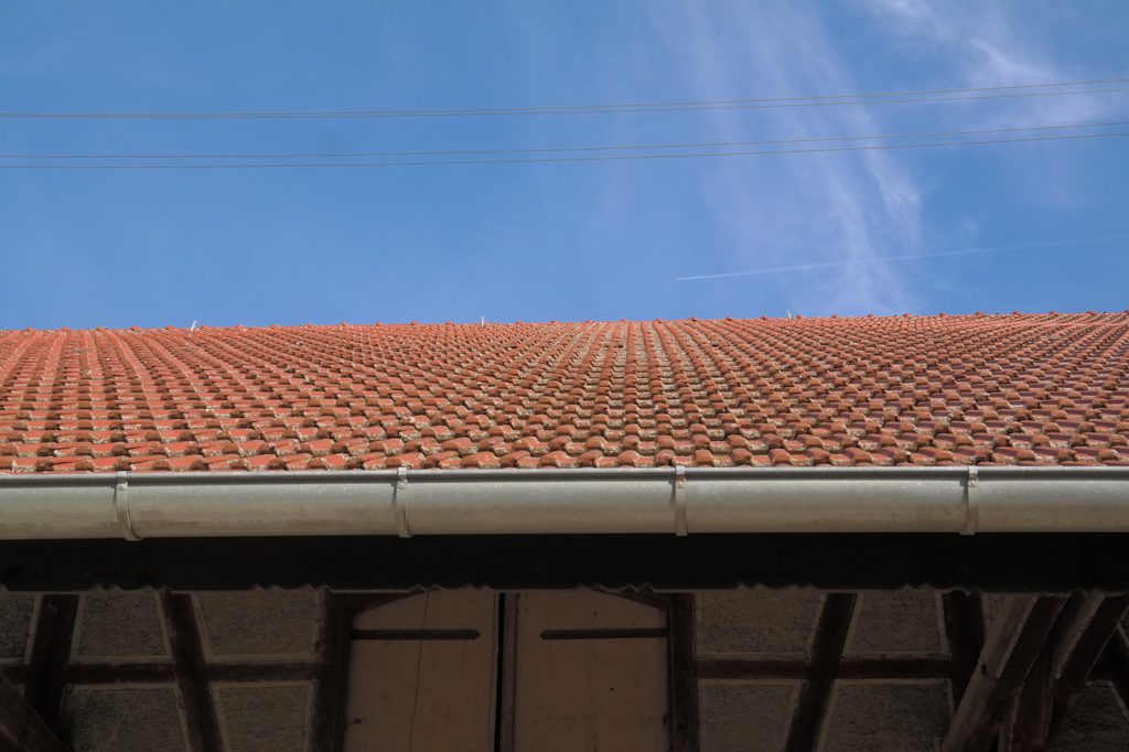 Terracotta tiled roof with metal guttering under a clear blue sky